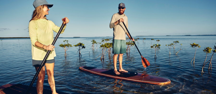 Man and woman paddle boarding while wearing UPF apparel